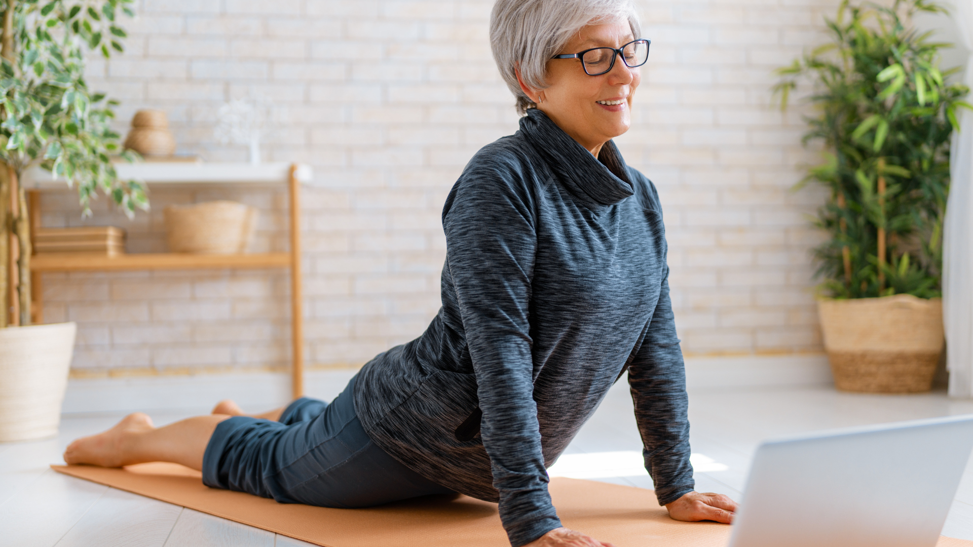 Senior woman in activewear watching online courses on laptop while exercising at home.