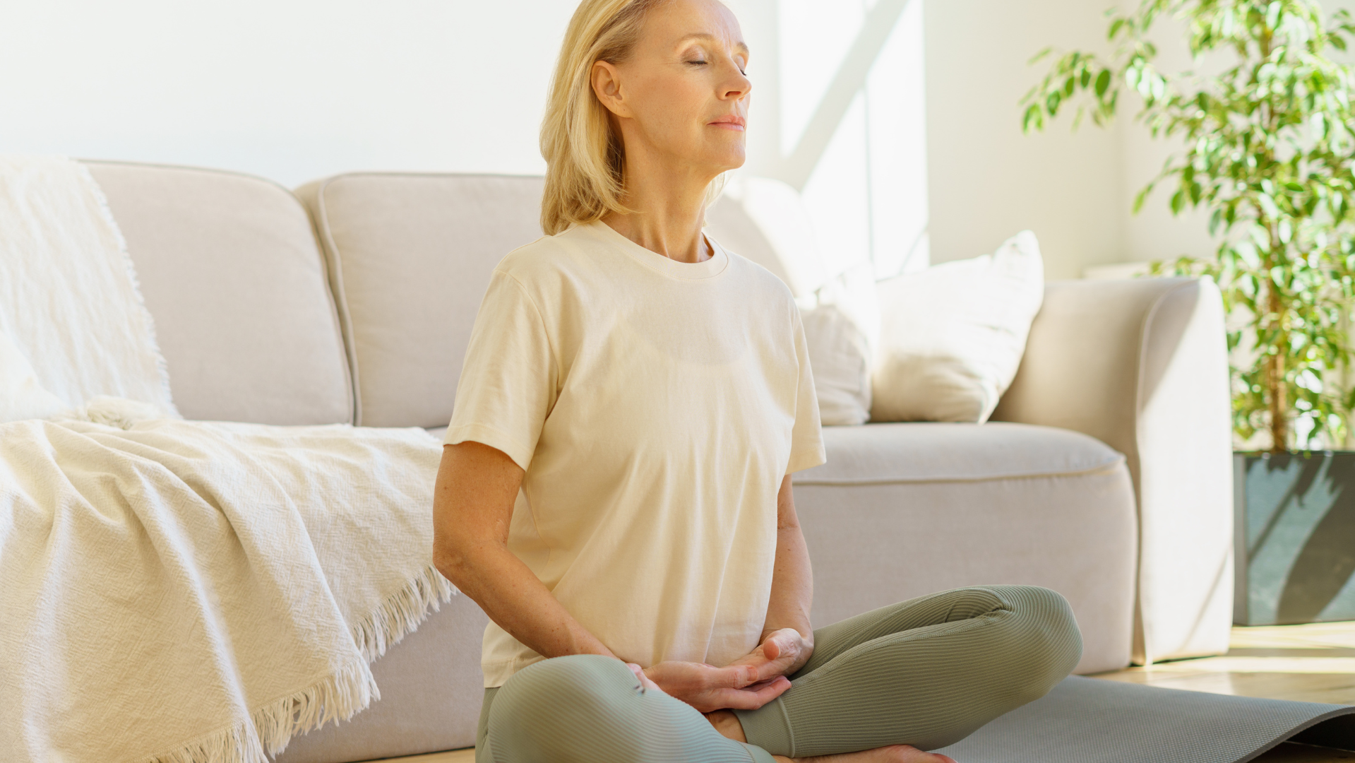 Peaceful senior woman in Lotus Pose and meditation with closed eyes at home while sitting on yoga mat on floor, practicing Diaphragm breathing.