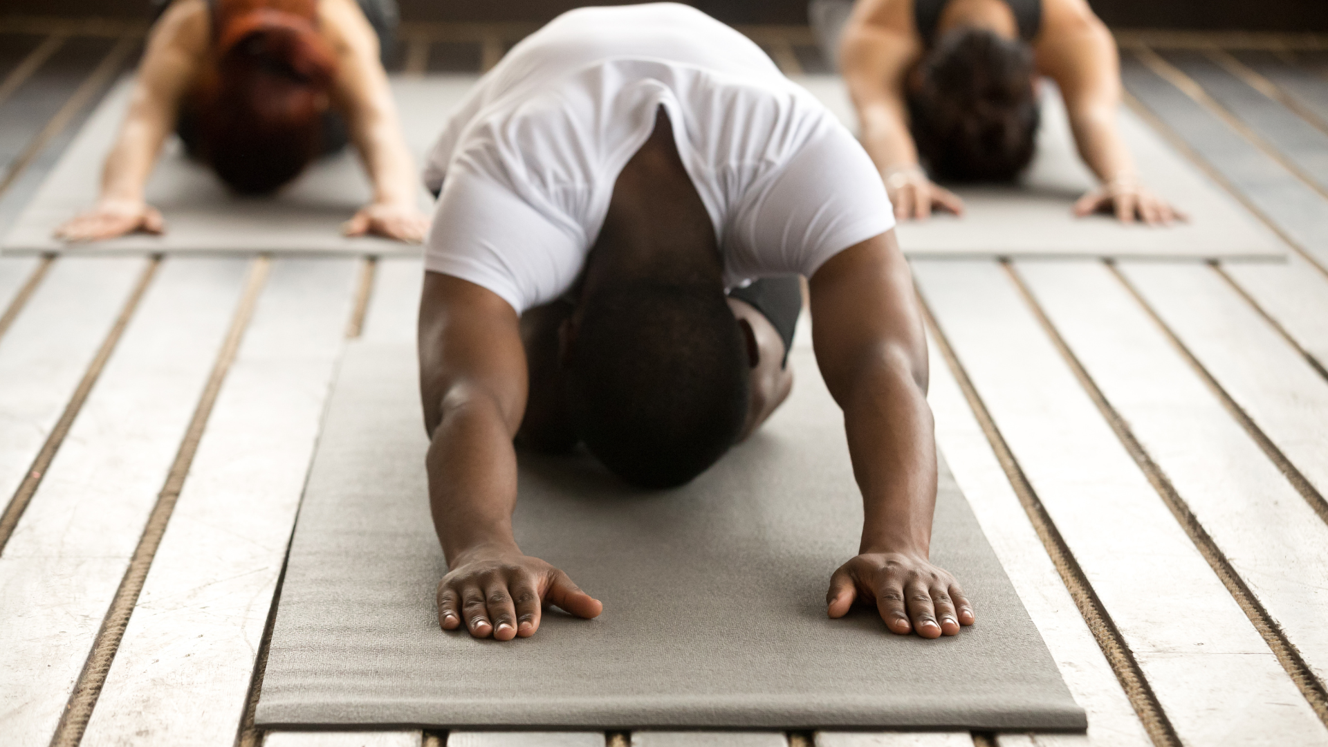 Young black man and group of yoga students practicing yoga lwith instructor, stretching in Child's Pose also known as Balasana, a gentle and sustainable pose.