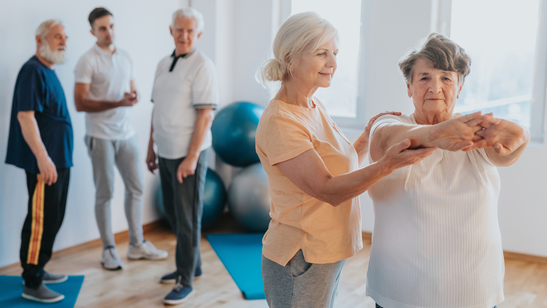 Senior yoga instructor helping another older woman with stretching.