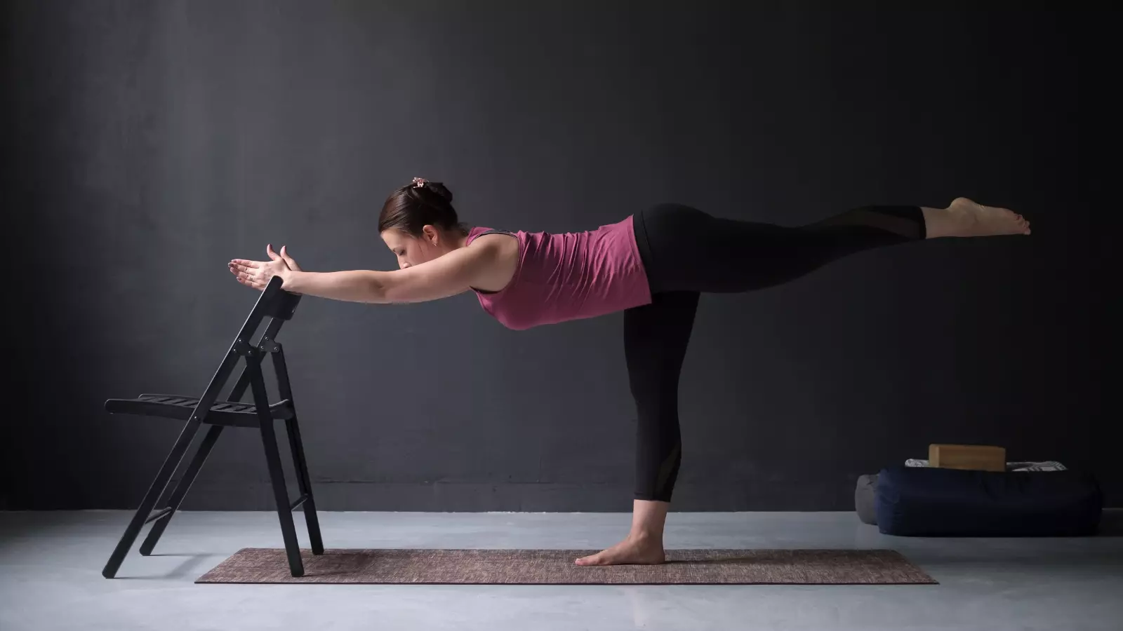 Warrior lll yoga pose. Woman show warrior asana using chair in studio background for a yoga stretch break when you can grab a chair.