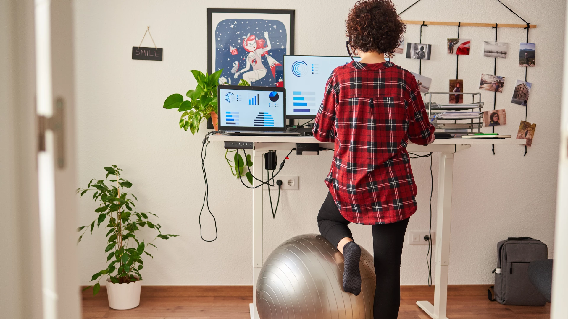 Woman working standing from home with an adjustable height desk and resting her knee on a fitball.