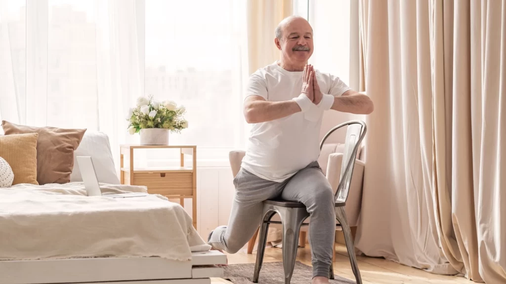 Elderly man practicing yoga asana warrior pose using chair—concept of how yoga may help dementia and Alzheimer's