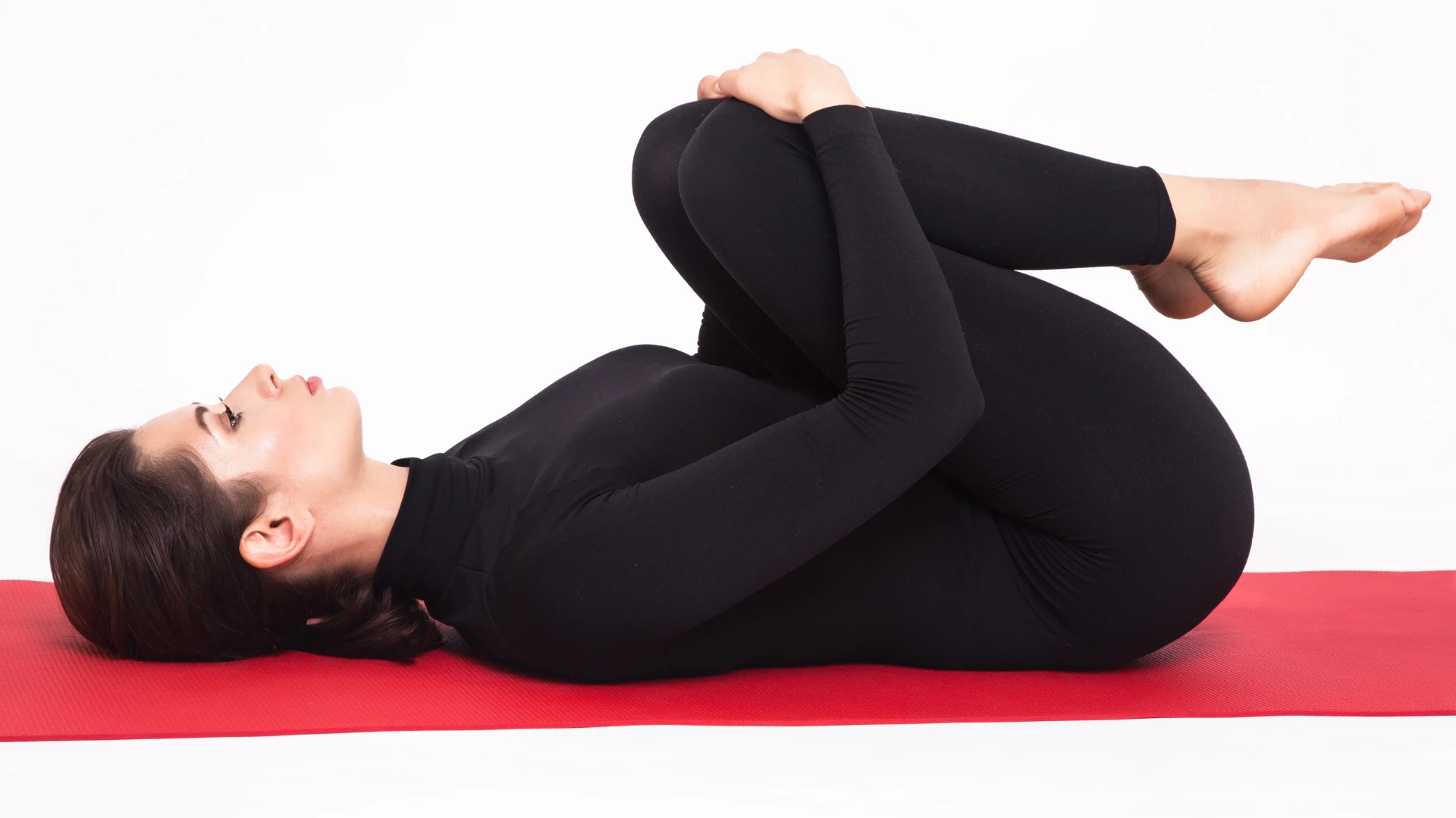 Yogi in black suit practicing yoga's. Apanasana pose. 