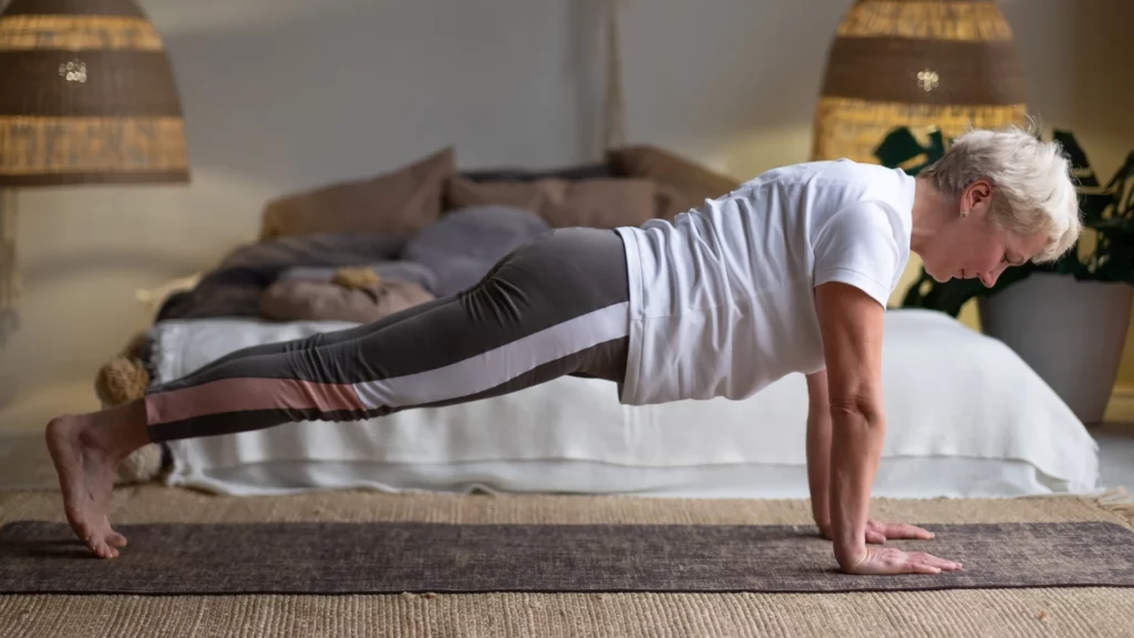 Senior woman working out indoors practicing Plank Pose to increase respiratory health and lung capacity.