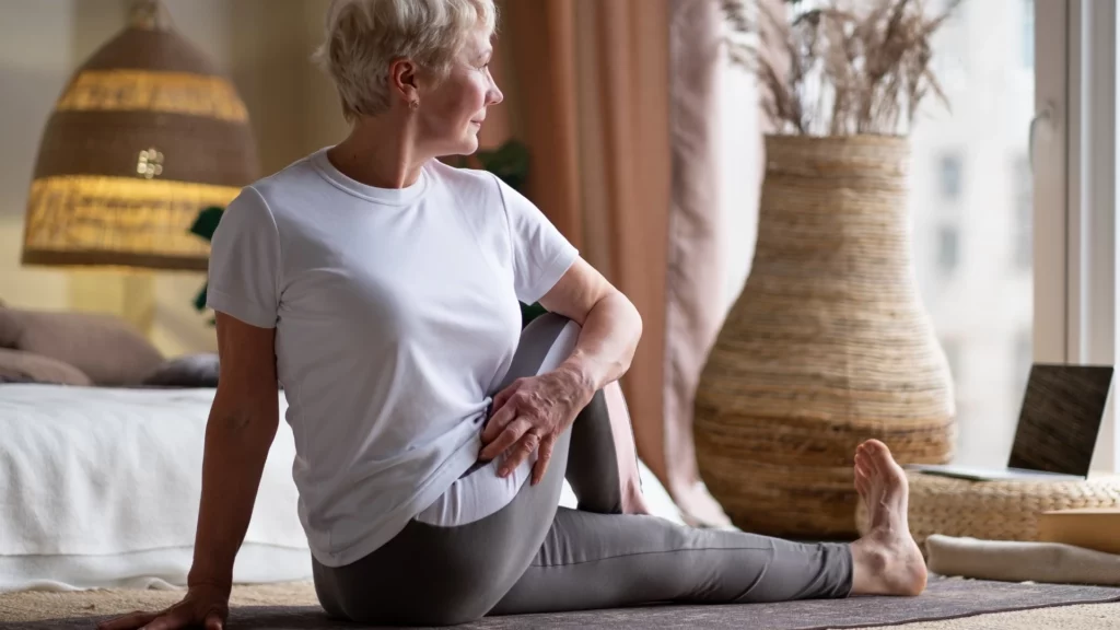 Senior woman practicing Seated Half Spinal Twist Pose or Ardha Matsyendrasana Pose which is a helpful pose for practicing healthy breathing exercises to increase lung capacity.