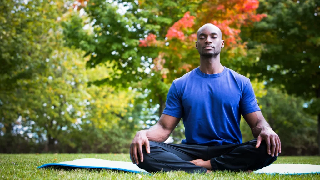 Young black man in the park practicing Pranayama or easy healthy breathing practices which can improve lung capacity and respiratory health.