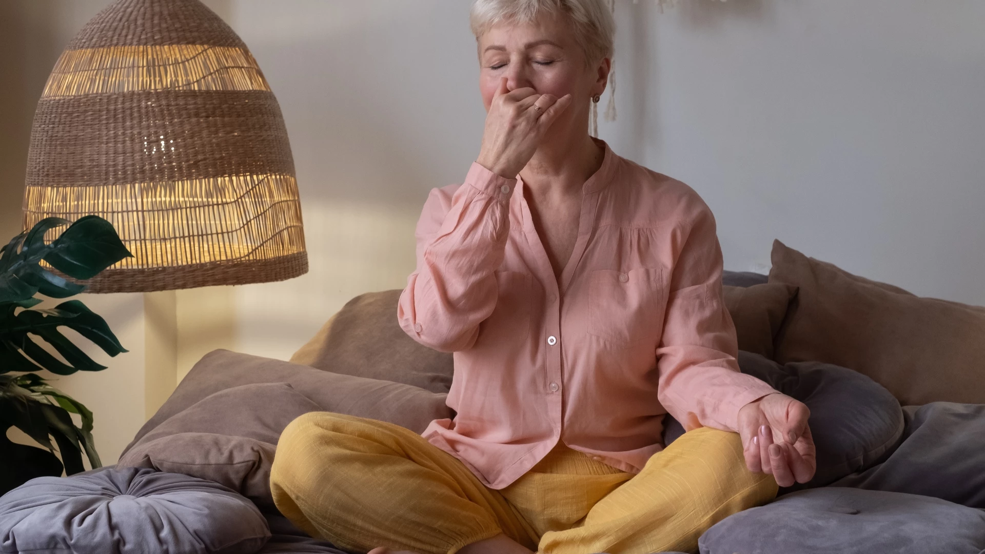 Senior woman practicing yoga at home, making Alternate Nostril Breathing exercise, nadi shodhana pranayama. Breath work for increased lung capacity