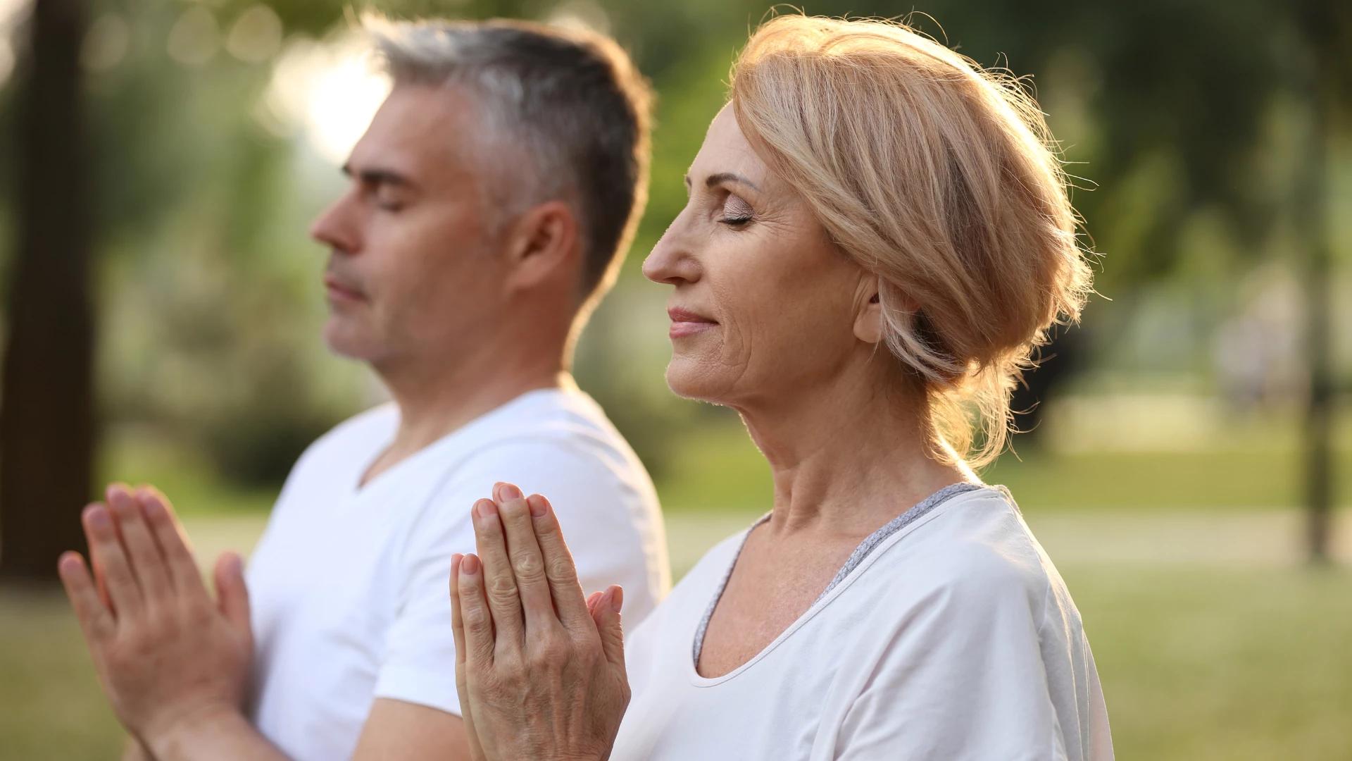 Couple practicing yoga in park at morning that can help alleviate mental suffering.