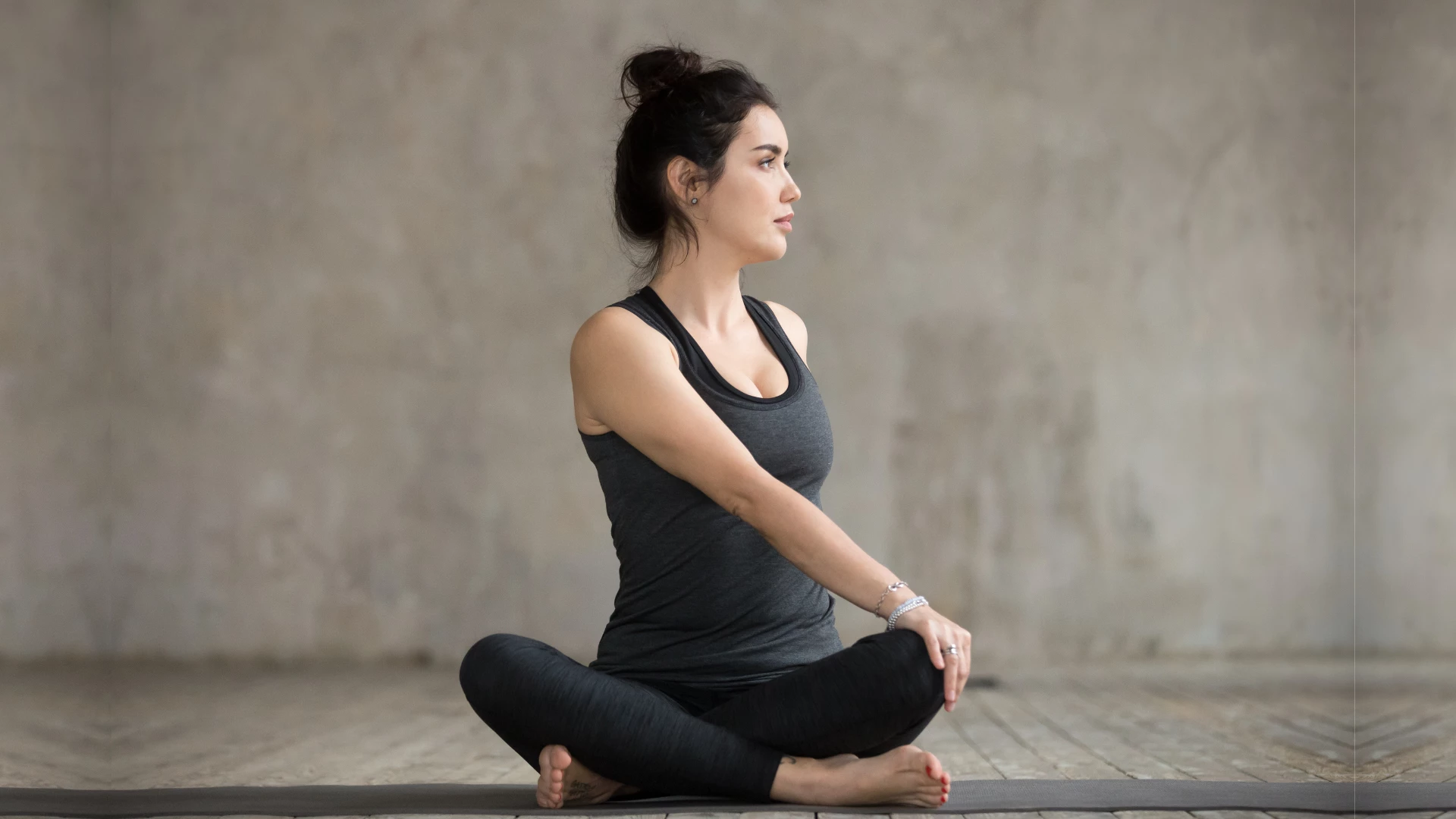 Young woman practicing yoga's Revolved Easy Pose also known as Parivrtta Sukhasana Pose. 