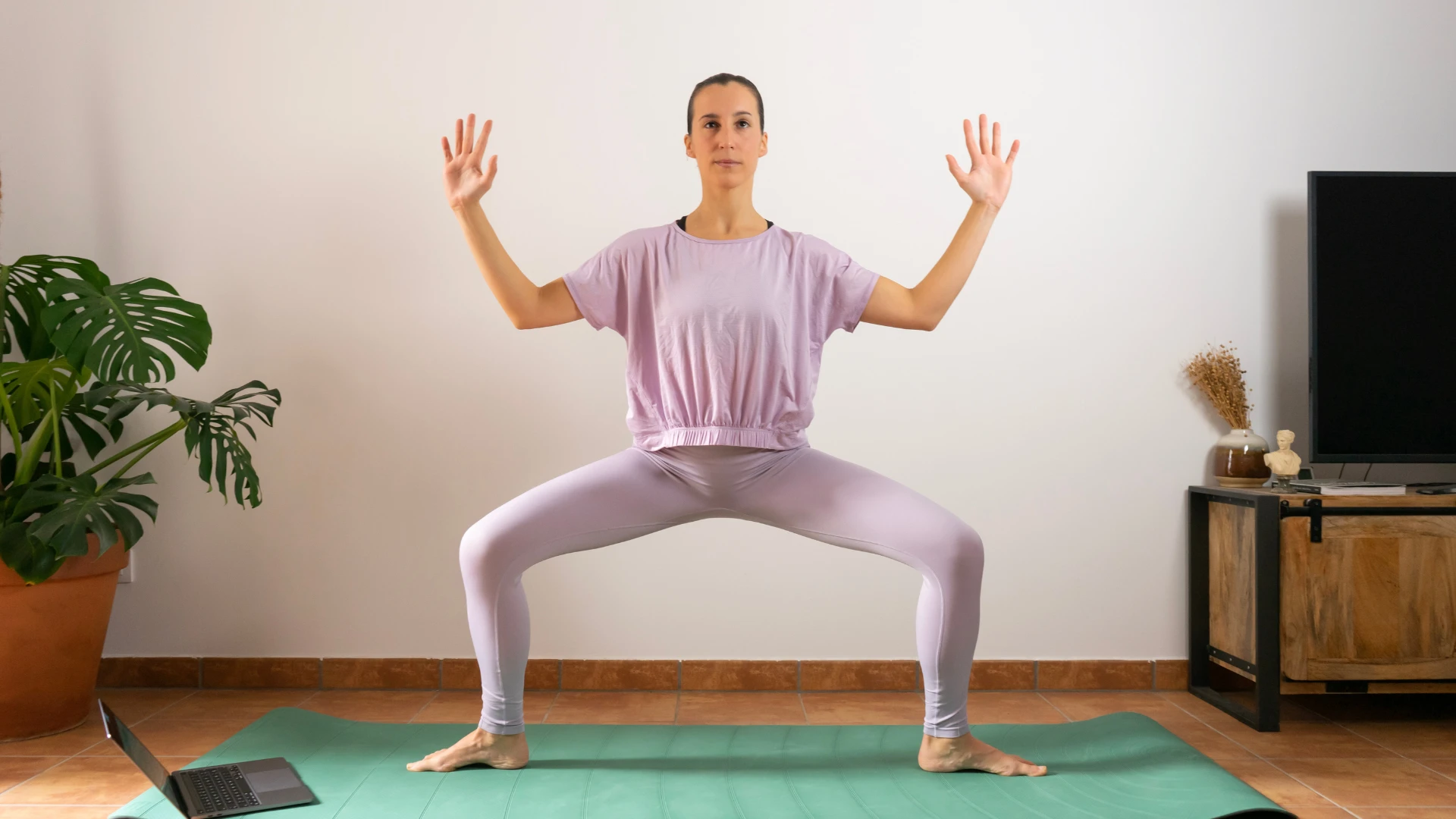 Woman practicing yoga at home in a wide-legged pose, showing how yoga and gene expression support strength, balance, and cellular transformation.